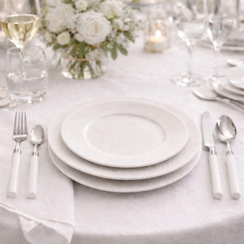 set posate 24 pezzi in acciaio inox con manico taupe - foto 4 Set posate in uso su tavola apparecchiata con piatti bianchi, bicchieri e vaso di fiori su tovaglia bianca